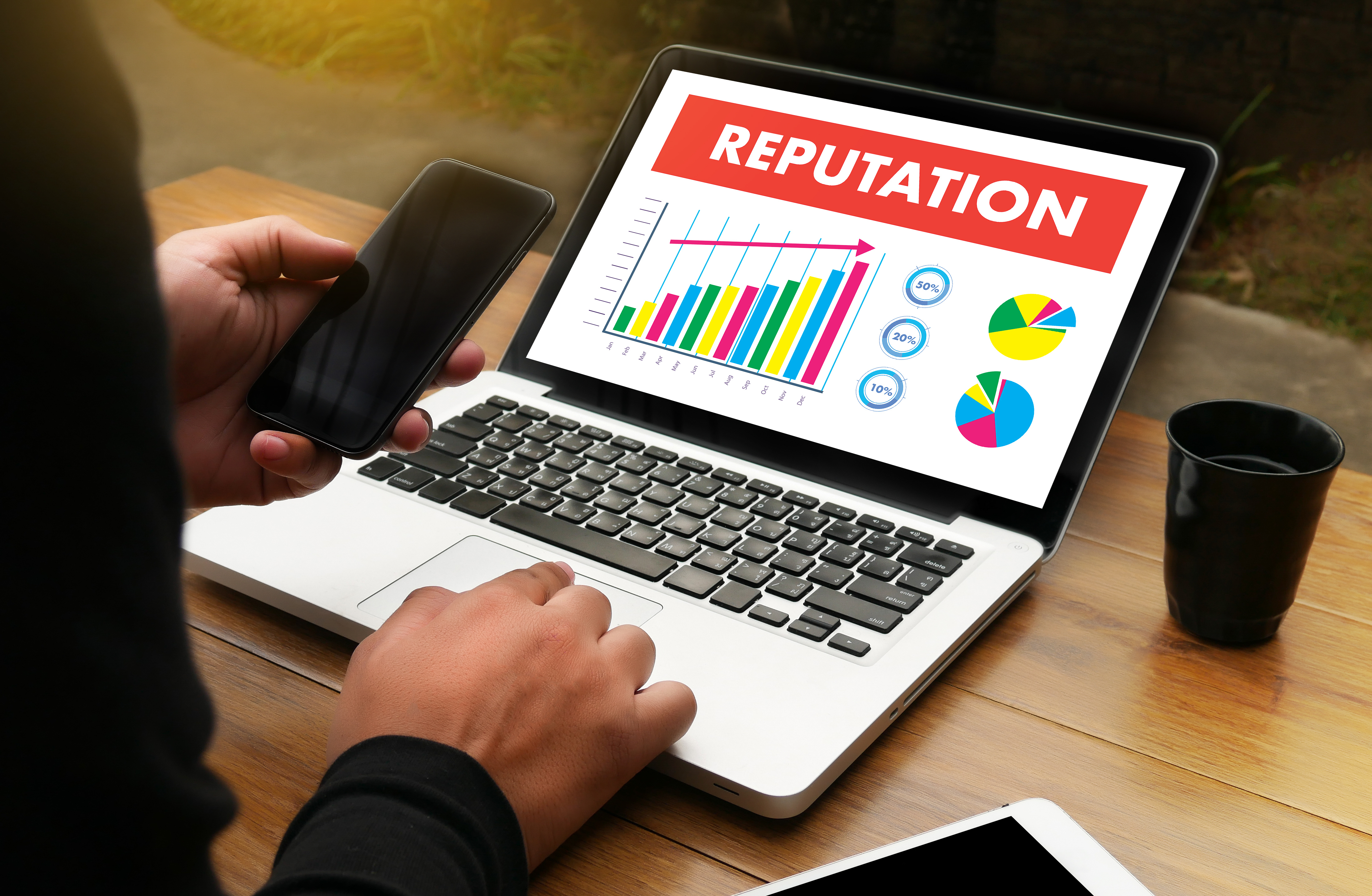 Person looking at phone with open laptop showing reputation projection graphs