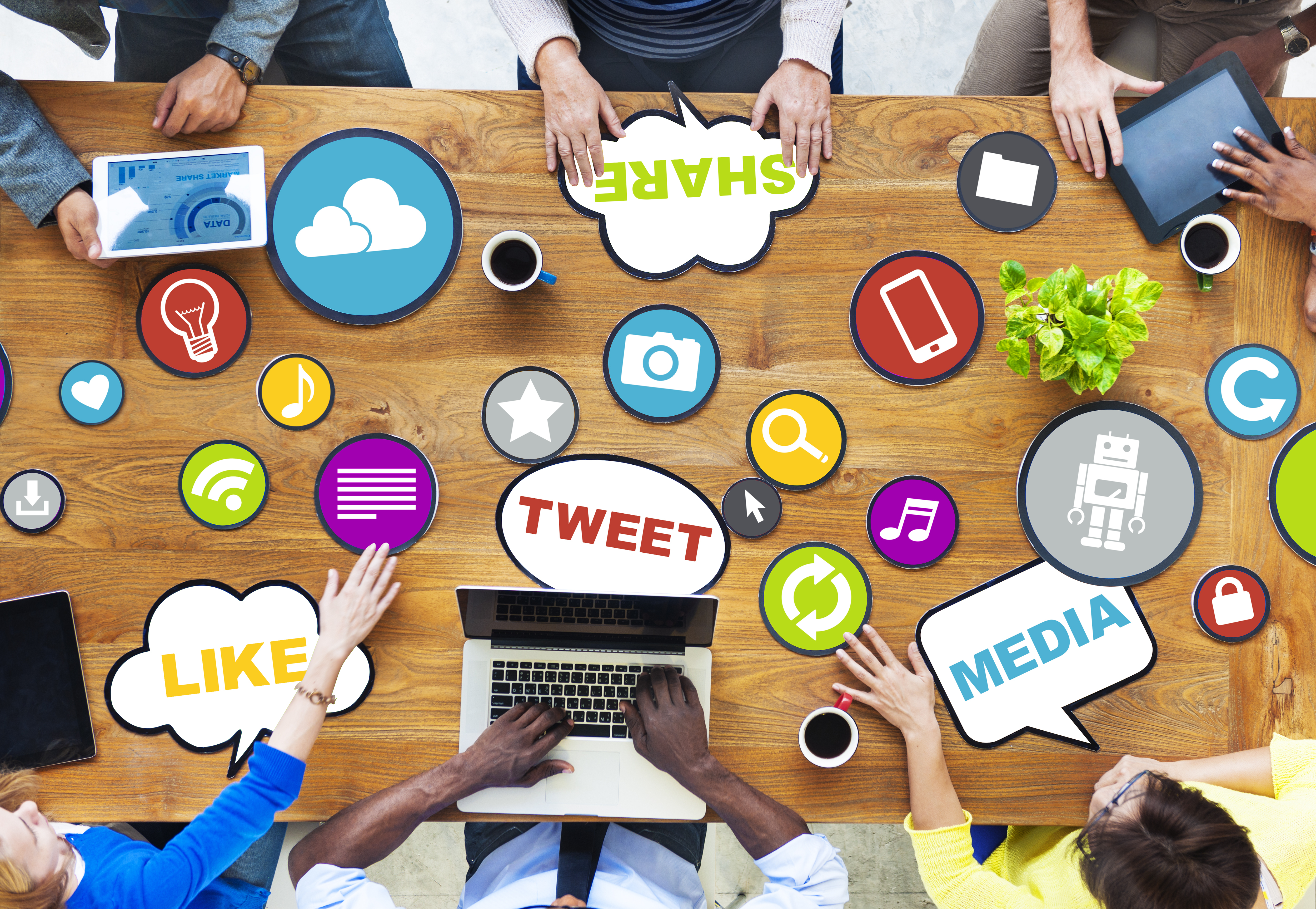 A group of people with devices sitting around a table littered with social media toon icons